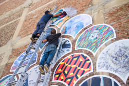 Deux artistes urbains composant une mosaïque de stickers géants en forme de goutte d’eau japonaise.